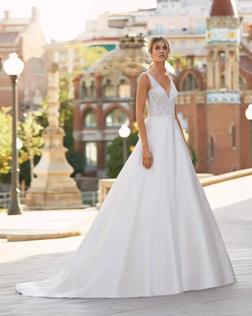 Mulher posando com vestido de noiva branco, de parte superior rendada e decote em formato vê, olhando para o horizonte. 