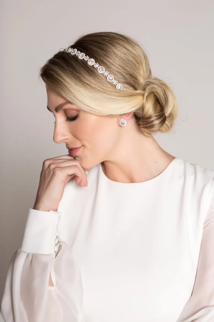 Mulher posando em vestido de noiva minimalista, com a mão direita apoiada sobre o queixo, e tiara posicionada sobre o cabelo.