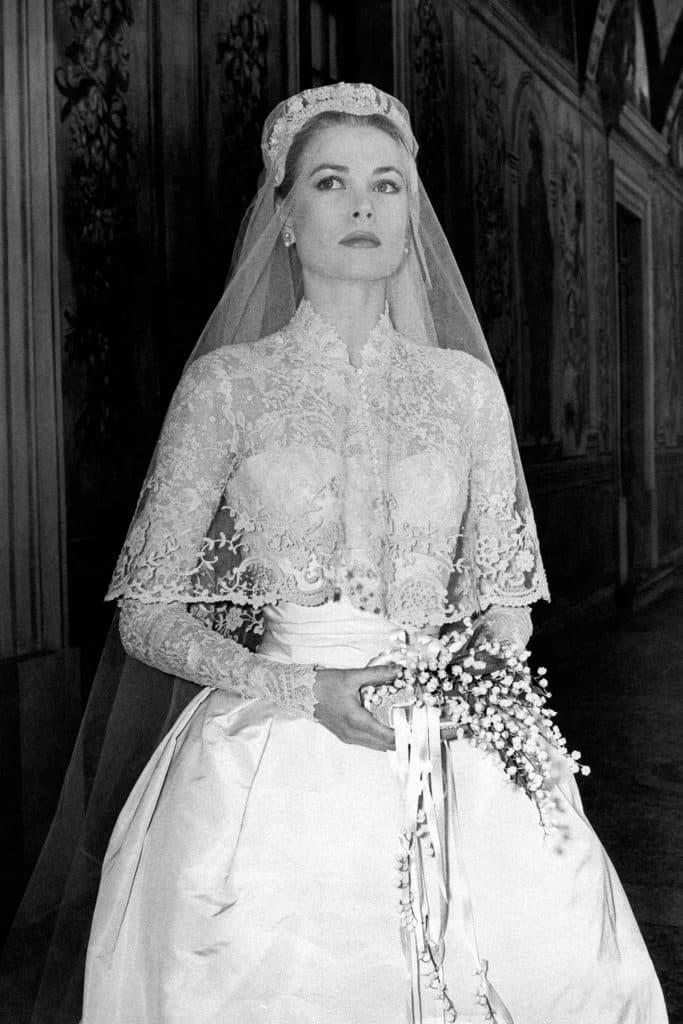 Fotografia em branco e preto de Grace Kelly, segurando buquê enquanto olha para o lado esquerdo, um véu cai sobre seu rosto.