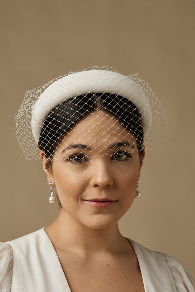 Mulher posa para foto, com seus cabelos presos, utilizando uma linda tiara Voilette em cor off-white.