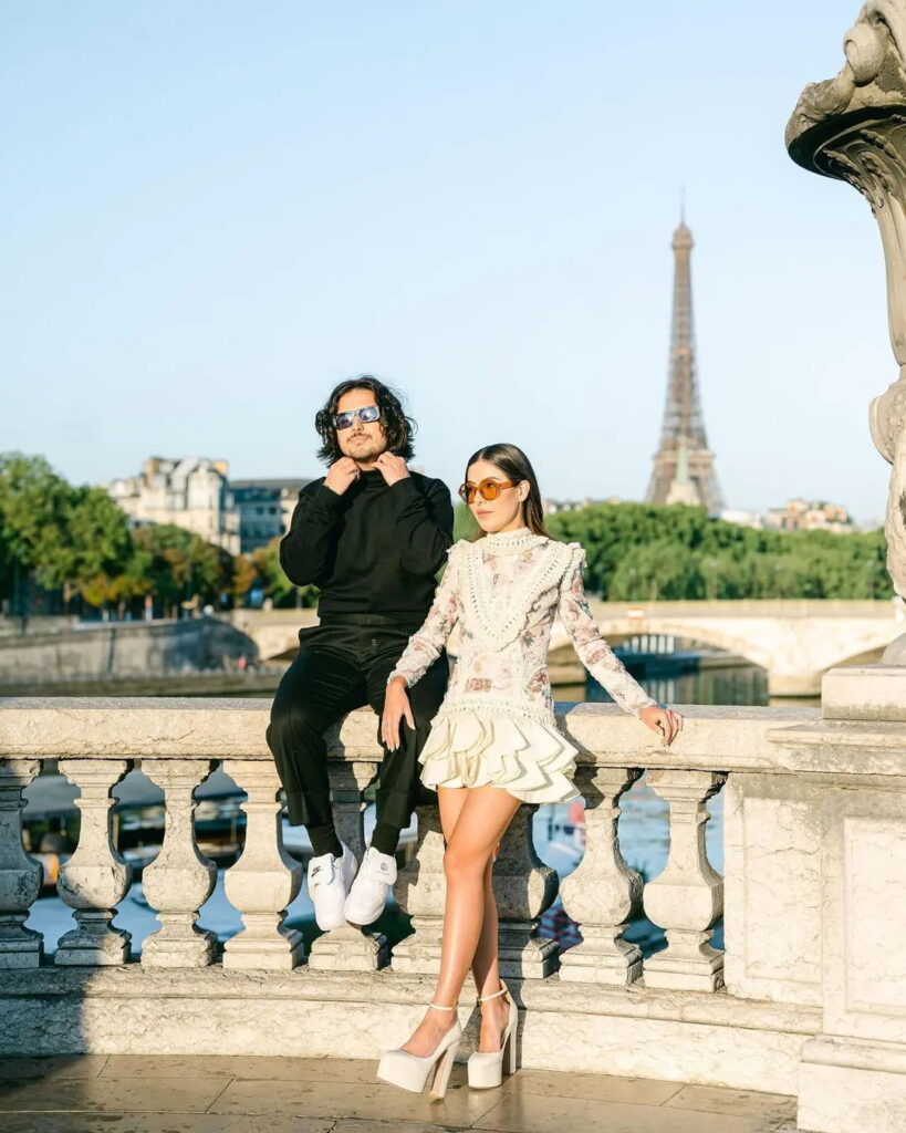Nath Araújo e Lucas Vivot posam para foto em frente à Torre Eiffel. Nath utilizando vestido Yolancris, o modelo é curto, com mangas longas.