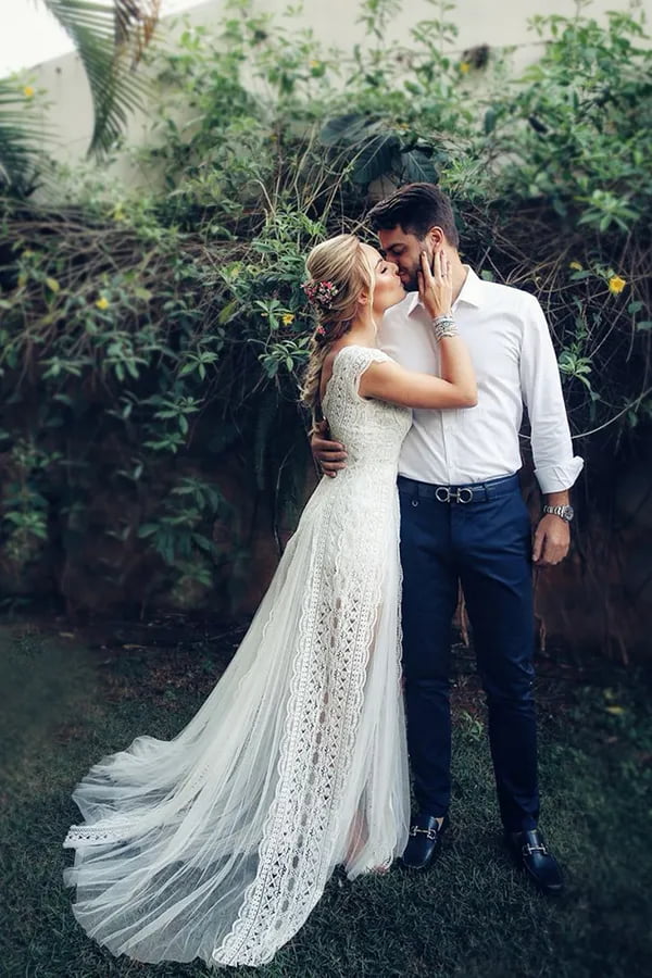 Layla Monteiro e William Naoum se beijam em foto. A noiva está usando um vestido Yolancris com saia confeccionada em tule bordado com renda e corpete trabalhado com alças de renda